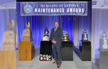 A picture of a men in a formal suits standing in front of many shiny awards