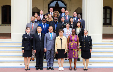 a picture of a group of men and women in formal attires and uniform standing in front of a white building