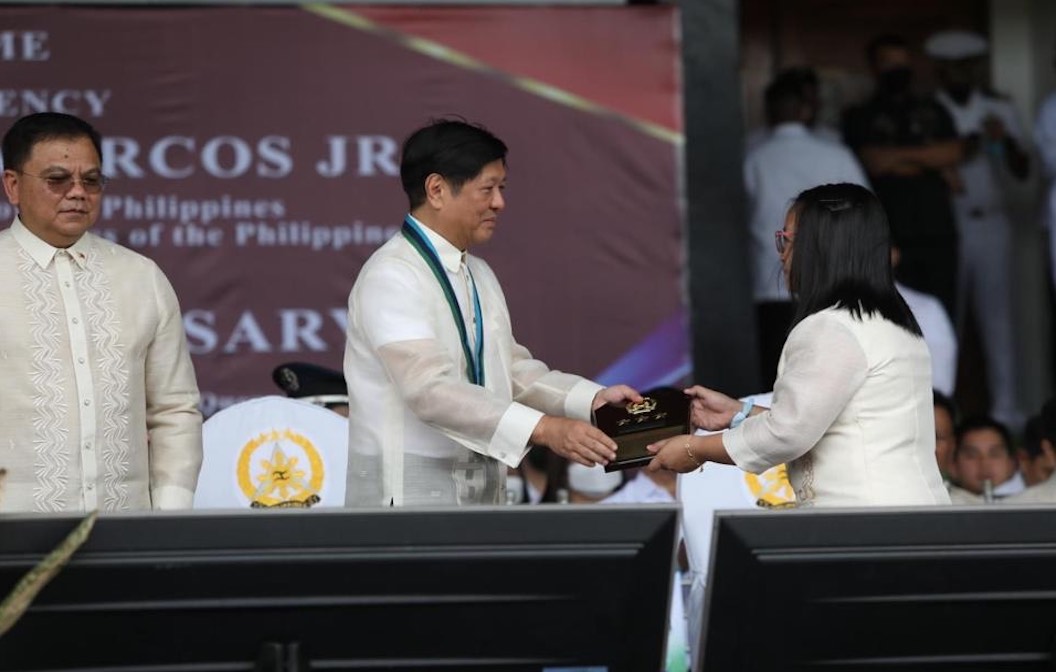 A picture of a man in a white collar shirt handing an award to a woman