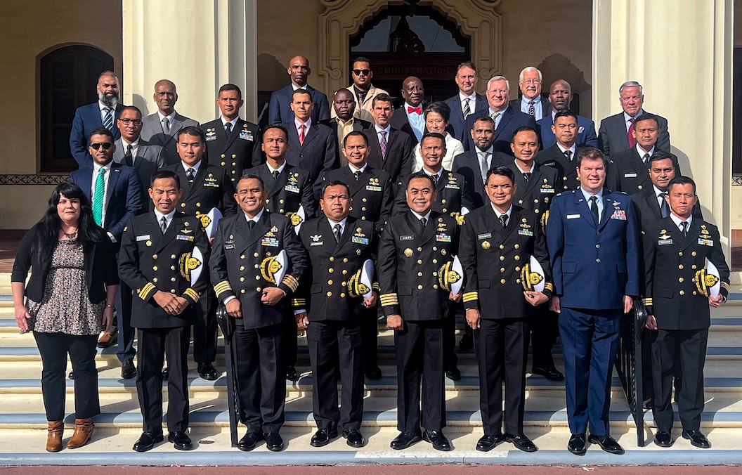 A group of 30 course participants, mostly male and in various country uniforms stand on the steps of the hotel at the Naval Postgraduate School.