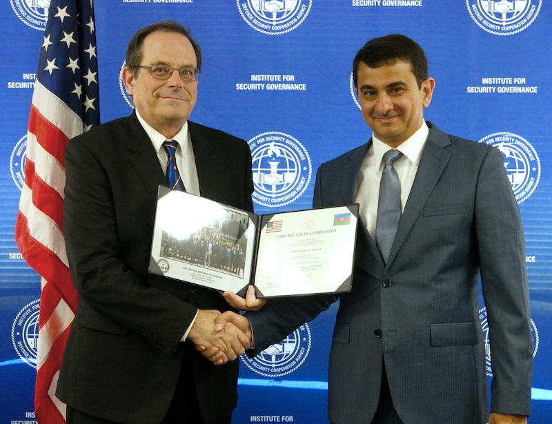 TWO MEN POSING IN FRONT OF BLUE SCREEN WITH ISG LOGO. ONE MAN IS HOLDING A CERTIFICATE WHILE THEY SHAKE HANDS