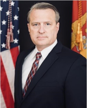 Man in a suit and tie standing in front of two flags