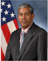 Man in a suit and tie standing in front of the U.S.A. flag