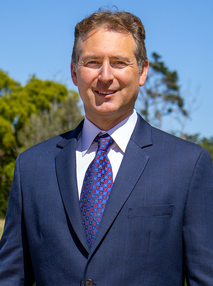 A picture of a man wearing navy suit with navy and red tie